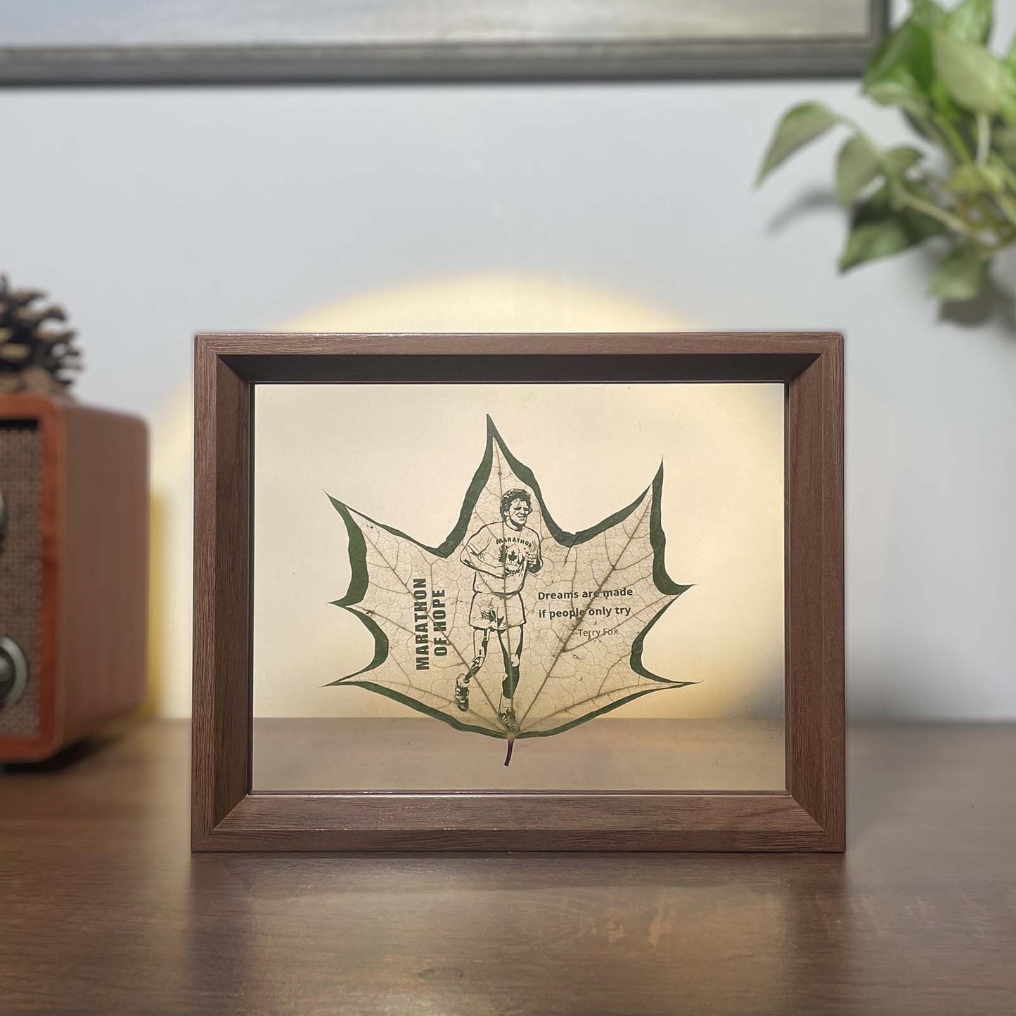 Framed artwork of a maple leaf carving of Terry Fox, on a wooden surface.