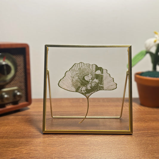 Decorative Ginkgo Leaf Art in a gold frame on a wooden surface with a vintage radio and plant in the background.