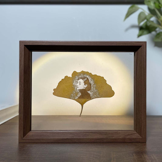 Framed artwork with a silhouette of Audrey Hepburn on a ginkgo leaf against a light background