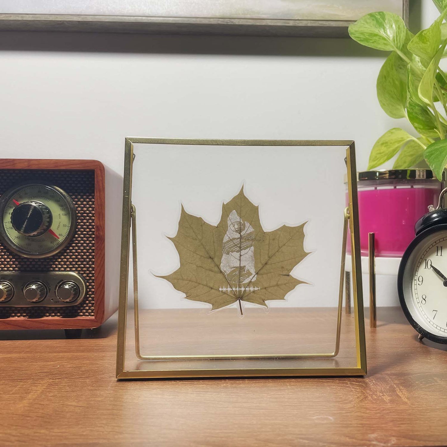 Framed maple leaf carving art on a wooden surface with a vintage radio and clock in the background.